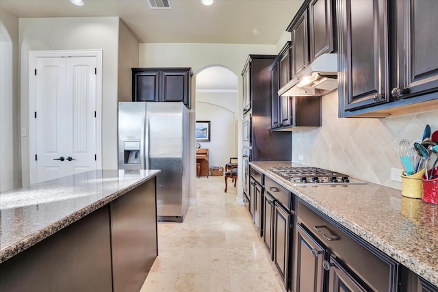 kitchen with tasteful backsplash, dark brown cabinetry, stainless steel appliances, and light stone countertops