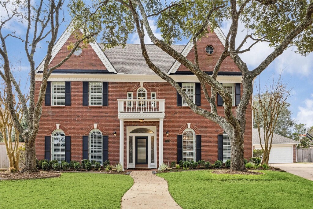 colonial home with brick siding, a front lawn, a detached garage, and a balcony