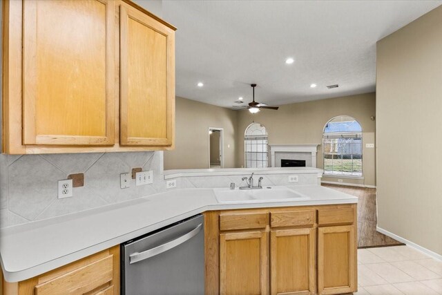 kitchen featuring light brown cabinets, light countertops, stainless steel dishwasher, and a sink