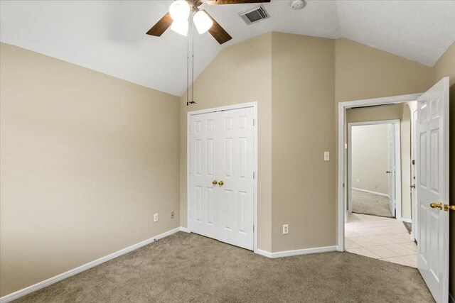 unfurnished bedroom with baseboards, visible vents, light colored carpet, lofted ceiling, and a closet