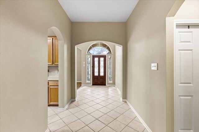 foyer featuring light tile patterned floors, arched walkways, and baseboards