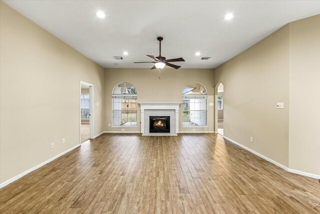 unfurnished living room with ceiling fan, a fireplace with flush hearth, wood finished floors, visible vents, and baseboards