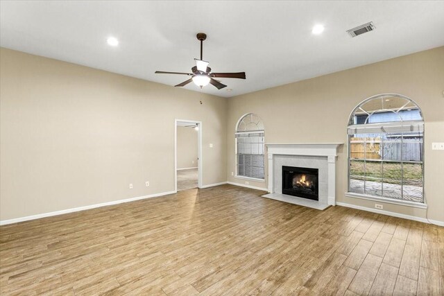 unfurnished living room featuring a ceiling fan, a fireplace with flush hearth, baseboards, and light wood finished floors