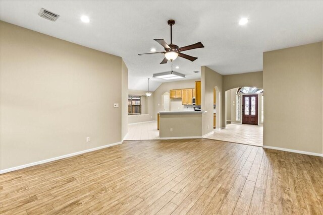 unfurnished living room with arched walkways, light wood finished floors, visible vents, ceiling fan, and baseboards