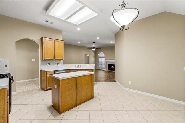 kitchen with arched walkways, light countertops, hanging light fixtures, brown cabinetry, and open floor plan