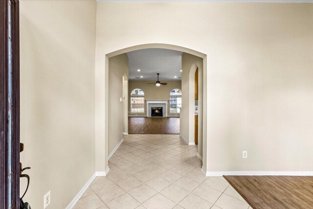 hallway with arched walkways, baseboards, and light tile patterned floors