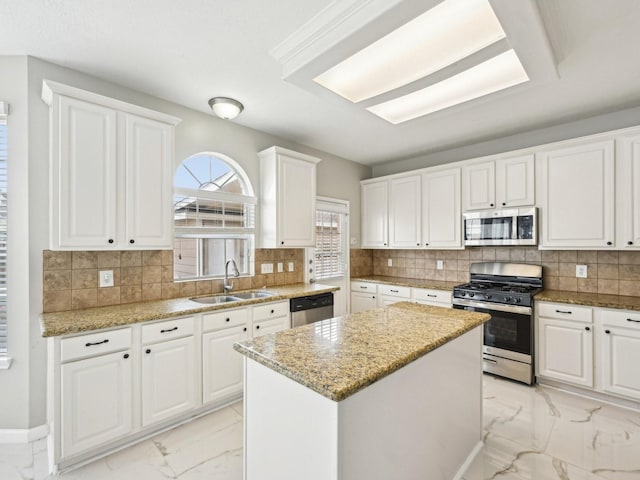 kitchen featuring sink, stainless steel appliances, light stone counters, white cabinets, and a kitchen island