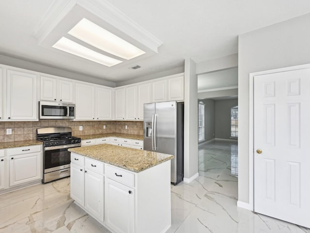 kitchen featuring a kitchen island, appliances with stainless steel finishes, white cabinets, backsplash, and light stone counters