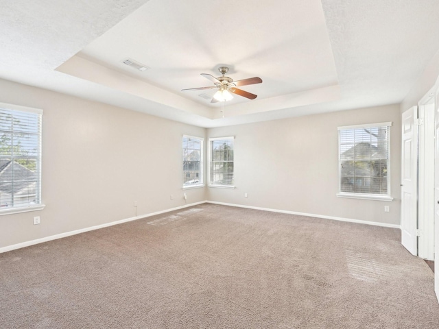 carpeted empty room featuring ceiling fan and a raised ceiling