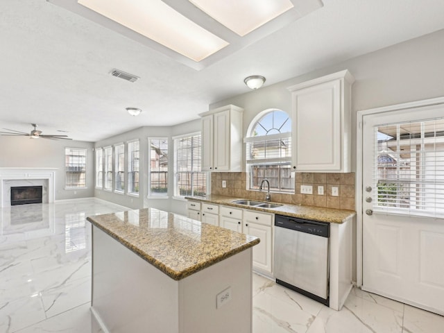 kitchen with sink, white cabinetry, light stone counters, a kitchen island, and stainless steel dishwasher