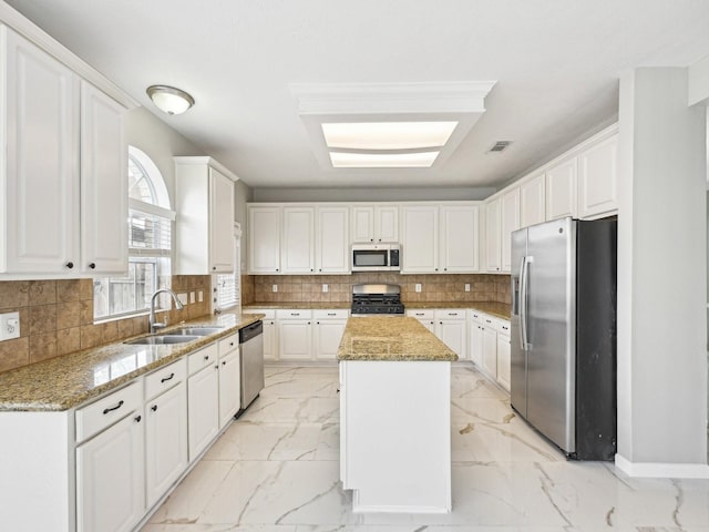 kitchen with sink, white cabinetry, a kitchen island, stainless steel appliances, and light stone countertops