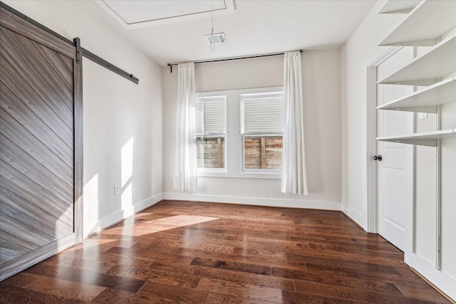 empty room featuring a barn door and dark wood-type flooring