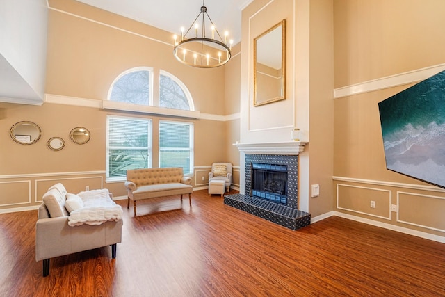 living room with a high ceiling, hardwood / wood-style floors, a tile fireplace, and a notable chandelier