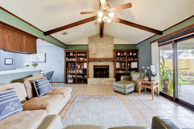 tiled living room featuring ceiling fan, lofted ceiling with beams, a brick fireplace, and a textured ceiling