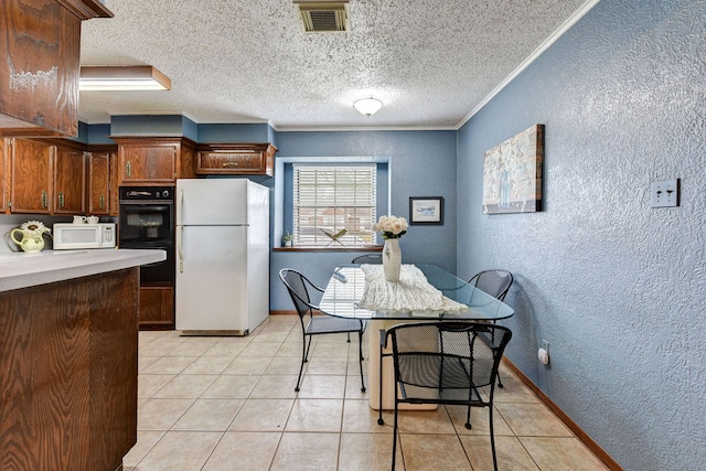 kitchen with light tile patterned floors, white appliances, ornamental molding, and a textured ceiling