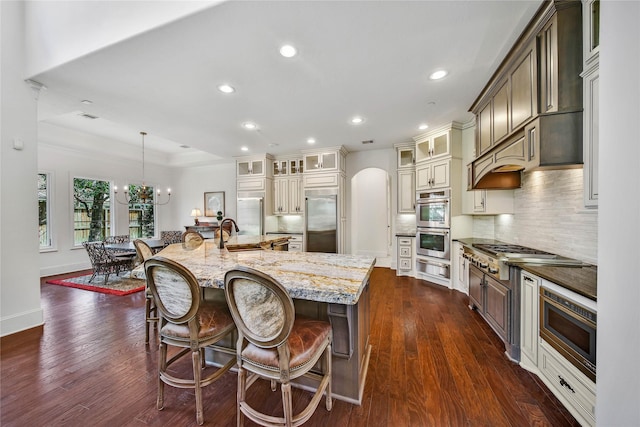 kitchen featuring a spacious island, a breakfast bar area, built in appliances, pendant lighting, and light stone countertops