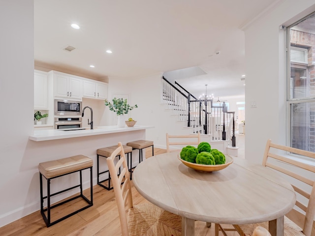 dining room with an inviting chandelier, crown molding, sink, and light hardwood / wood-style flooring