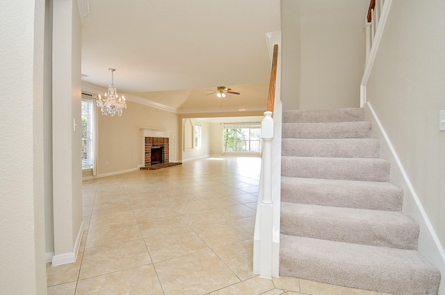 stairs featuring tile patterned flooring, crown molding, ceiling fan with notable chandelier, and a fireplace