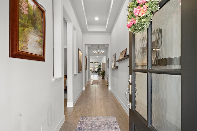 hall with a raised ceiling, wood-type flooring, and an inviting chandelier