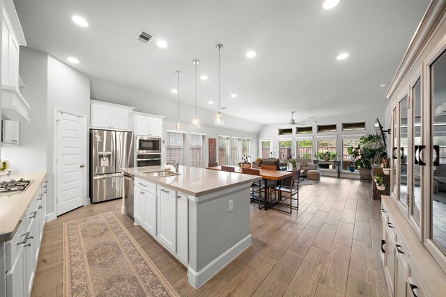 kitchen with white cabinetry, appliances with stainless steel finishes, decorative light fixtures, and an island with sink