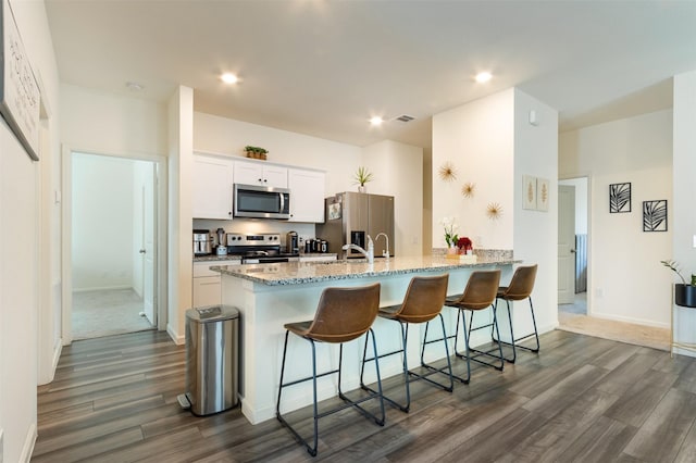 kitchen featuring dark hardwood / wood-style floors, a breakfast bar area, white cabinets, kitchen peninsula, and stainless steel appliances