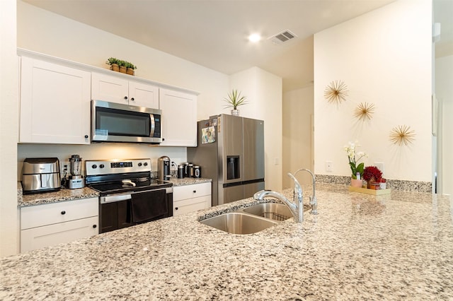 kitchen featuring stainless steel appliances, white cabinetry, light stone countertops, and sink