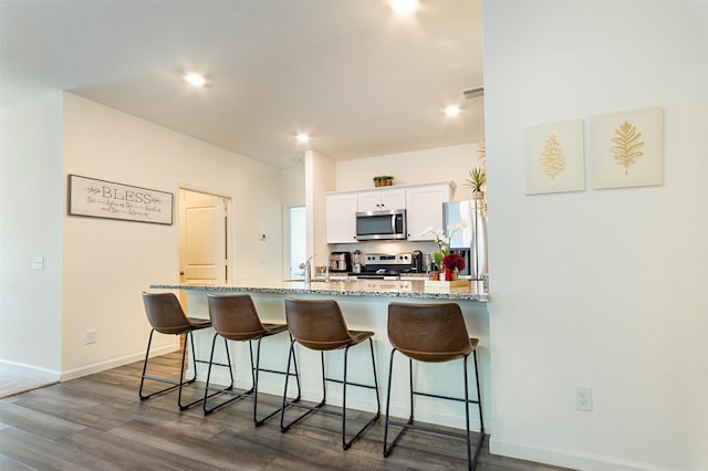 kitchen featuring appliances with stainless steel finishes, a kitchen bar, light stone countertops, and white cabinets