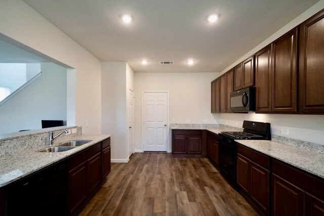 kitchen with sink, dark wood-type flooring, light stone counters, and black appliances