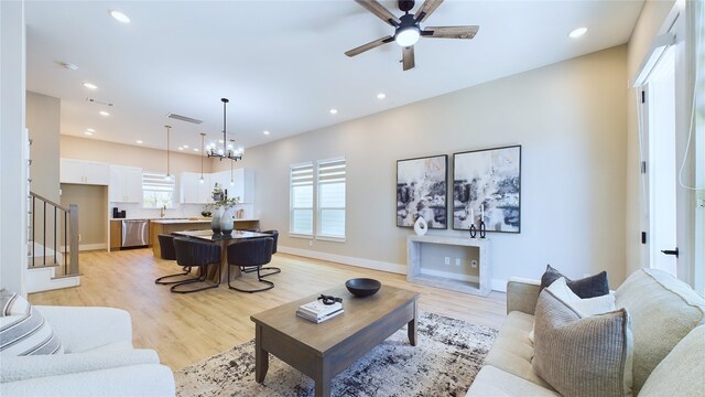 living room featuring ceiling fan with notable chandelier, light hardwood / wood-style floors, and a wealth of natural light