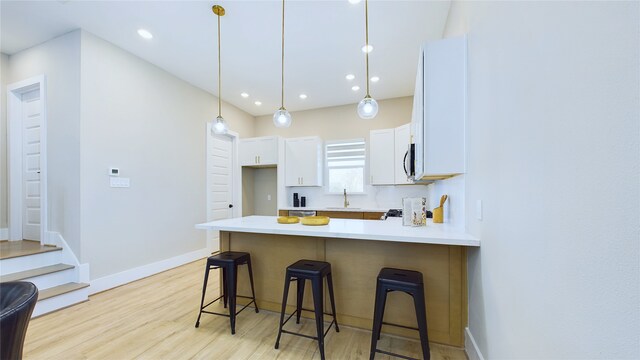 kitchen featuring a breakfast bar, pendant lighting, sink, white cabinets, and light wood-type flooring