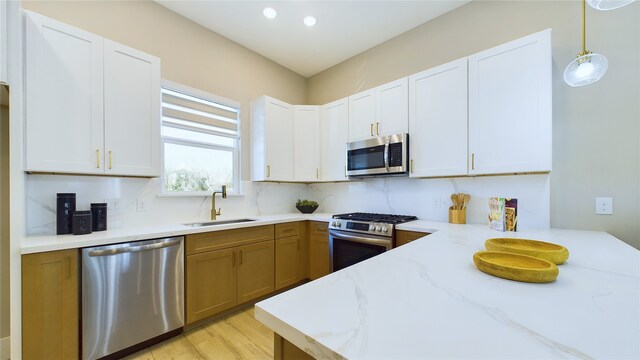 kitchen with sink, pendant lighting, stainless steel appliances, light stone countertops, and white cabinets