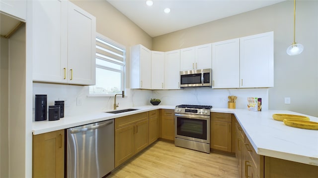 kitchen with stainless steel appliances, white cabinetry, sink, and pendant lighting