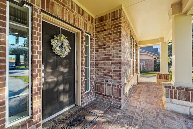 view of exterior entry with brick siding and a porch