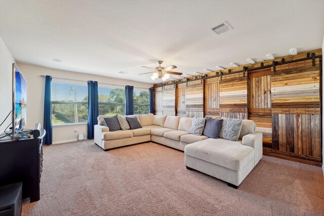 living room featuring a barn door, ceiling fan, and carpet flooring