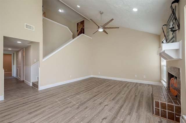 unfurnished living room featuring high vaulted ceiling, a fireplace, ceiling fan, a textured ceiling, and light wood-type flooring