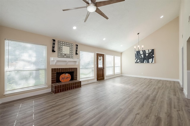 unfurnished living room featuring hardwood / wood-style flooring, lofted ceiling, ceiling fan with notable chandelier, and a brick fireplace