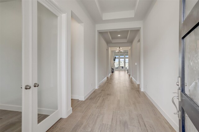 hallway with a raised ceiling, a chandelier, and light wood-type flooring