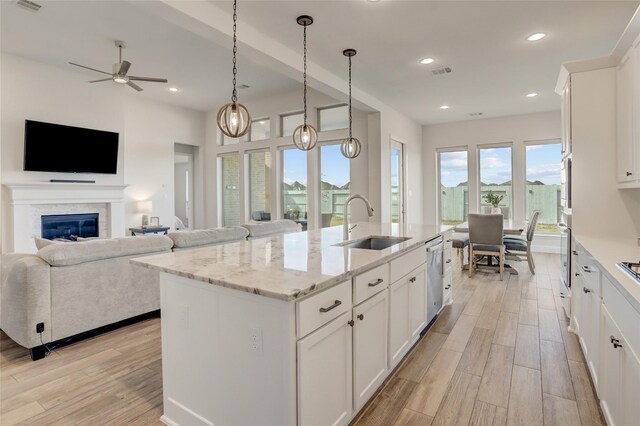 kitchen featuring sink, light stone counters, a center island with sink, pendant lighting, and white cabinets