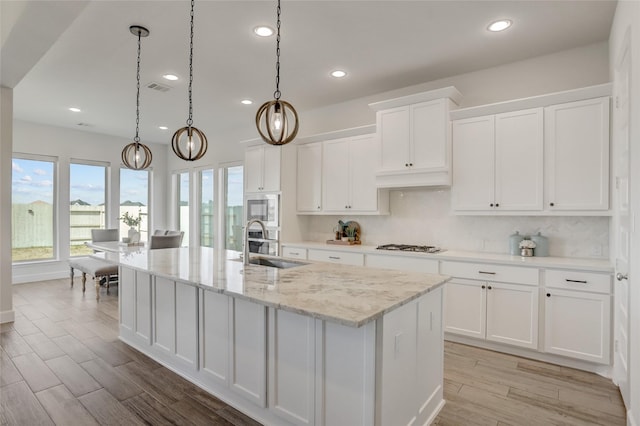 kitchen featuring tasteful backsplash, an island with sink, white cabinets, and decorative light fixtures