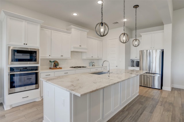 kitchen with a kitchen island with sink, stainless steel appliances, a sink, white cabinetry, and light wood finished floors