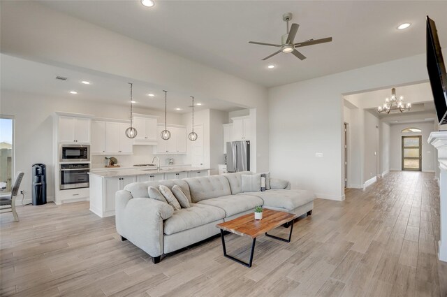 living room with ceiling fan with notable chandelier, sink, light hardwood / wood-style floors, and a wealth of natural light