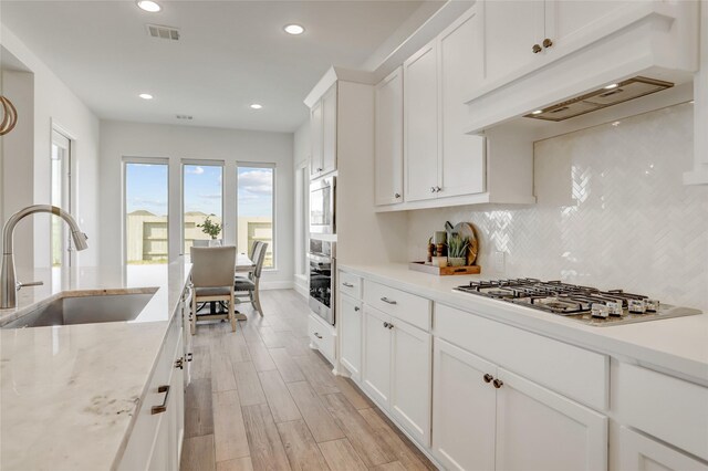 kitchen with stainless steel gas cooktop, visible vents, decorative backsplash, light wood-style floors, and a sink