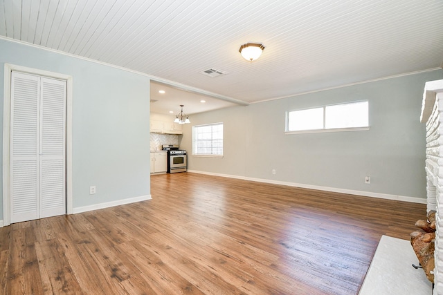 unfurnished living room featuring crown molding, an inviting chandelier, a stone fireplace, and hardwood / wood-style floors