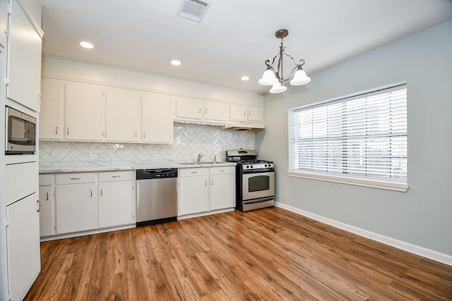 kitchen with stainless steel appliances, white cabinetry, hanging light fixtures, and backsplash