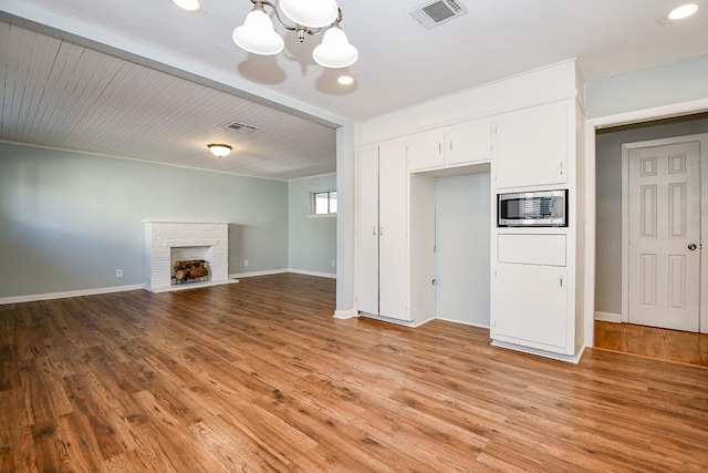 unfurnished living room featuring a chandelier, light hardwood / wood-style floors, and a brick fireplace