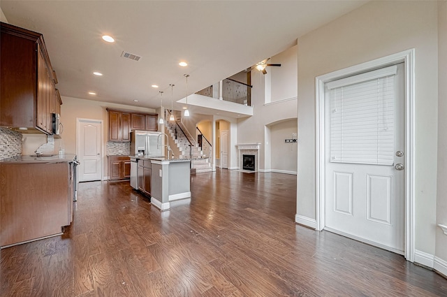 kitchen with appliances with stainless steel finishes, a kitchen island with sink, backsplash, dark hardwood / wood-style flooring, and decorative light fixtures