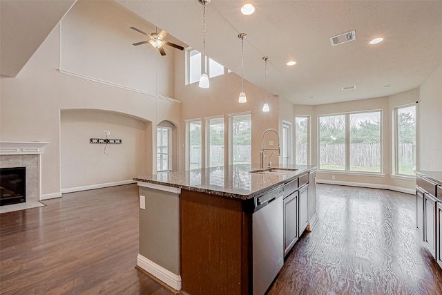 kitchen featuring dark wood-type flooring, sink, light stone counters, stainless steel dishwasher, and an island with sink