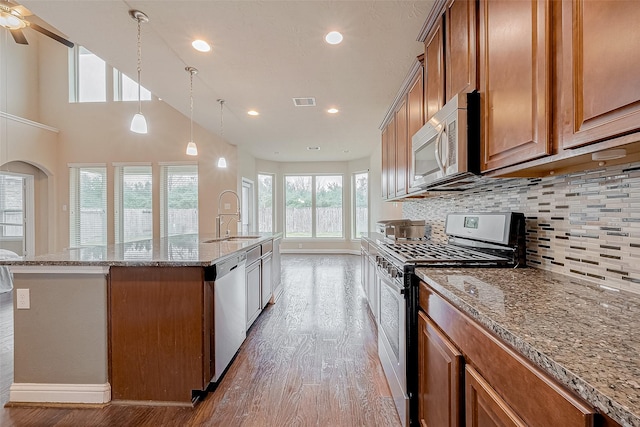 kitchen featuring an island with sink, sink, stainless steel appliances, light stone countertops, and light hardwood / wood-style flooring