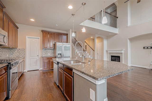 kitchen with sink, a center island with sink, appliances with stainless steel finishes, pendant lighting, and a fireplace