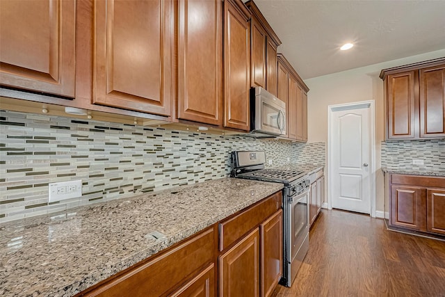 kitchen featuring appliances with stainless steel finishes, dark wood-type flooring, light stone counters, and decorative backsplash